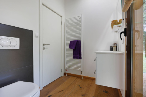 Baño moderno con suelo de madera, sanitarios blancos y radiador toallero en Woody Lodge Florian, Países Bajos.