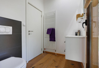 Baño moderno con suelo de madera, sanitarios blancos y radiador toallero en Woody Lodge Florian, Países Bajos.