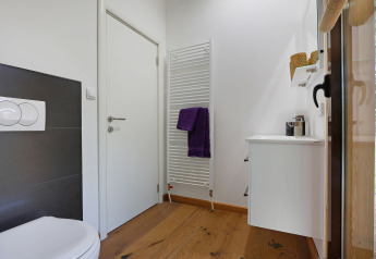 Moderne badkamer met houten vloer, witte voorzieningen en handdoekradiator bij Woody Lodge Florian, Nederland.