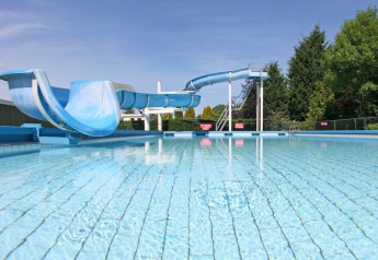 Buitenzwembad met blauwe waterglijbaan, zonnige dag op een glampinglocatie met groene omgeving.