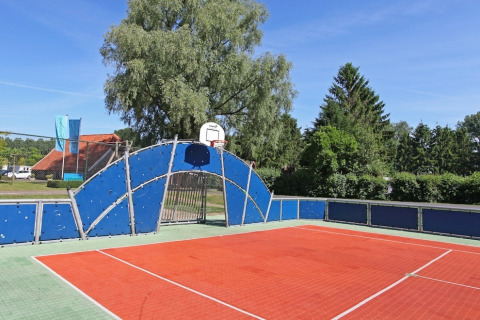 Udendørs basketballbane med blå stakit og grønne træer i baggrunden på et glamping-sted i Danmark.