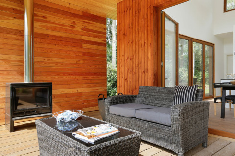 Accogliente area soggiorno con pareti in legno, caminetto e divano in vimini al Woody Lodge Valerie, Resort 't Schuttenbelt.
