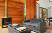 Sfeervolle zithoek met houten wanden, open haard, rotan bank en tafel in Woody Lodge Valerie, Resort 't Schuttenbelt.