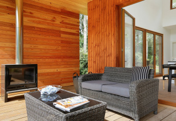 Sfeervolle zithoek met houten wanden, open haard, rotan bank en tafel in Woody Lodge Valerie, Resort 't Schuttenbelt.