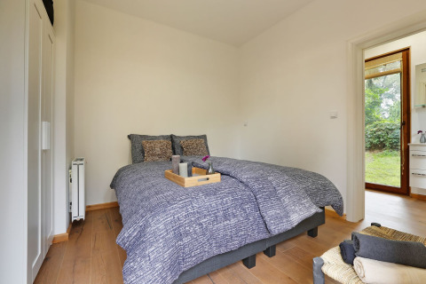 Dormitorio en Woody Lodge Valerie, Holiday Resort 't Schuttenbelt, Países Bajos, con cama doble y acceso al jardín.