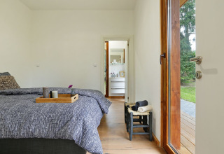 Slaapkamer in Woody Lodge Valerie op Holiday Resort 't Schuttenbelt met zicht op badkamer en tuin.