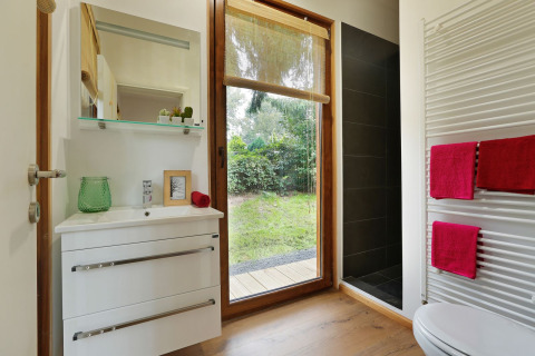 Baño moderno en Woody Lodge Valerie con ventana grande, vista a la naturaleza y toallas rojas vibrantes.
