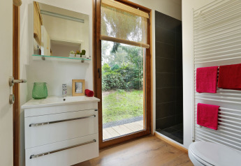 Baño moderno en Woody Lodge Valerie con ventana grande, vista a la naturaleza y toallas rojas vibrantes.
