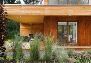 Modern tiny house Woody Lodge Valerie with wooden exterior, terrace and tall grasses at Dutch holiday resort.