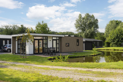 Moderne lodge aan een vijver op Holiday Park De Lochemse Berg in Nederland, met terras en natuurlijke omgeving.