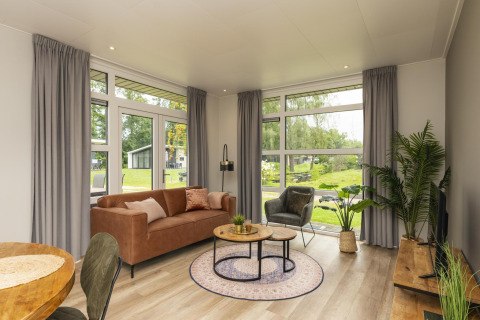 Living room of The Water Lily lodge at Holiday Park De Lochemse Berg in the Netherlands with modern decor and large windows.