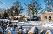 Cabañas nevadas en Lodge Mistique, Holiday Park De Lochemse Berg, Países Bajos, rodeadas de árboles invernales.