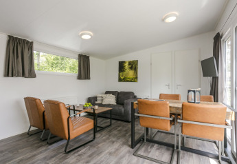 Woonkamer in Lodge Mistique op Vakantiepark De Lochemse Berg in Nederland, met bruine stoelen en bank.