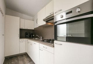 Cucina moderna nella Lodge Mistique, Holiday Park De Lochemse Berg, Paesi Bassi, con mobili bianchi e forno.
