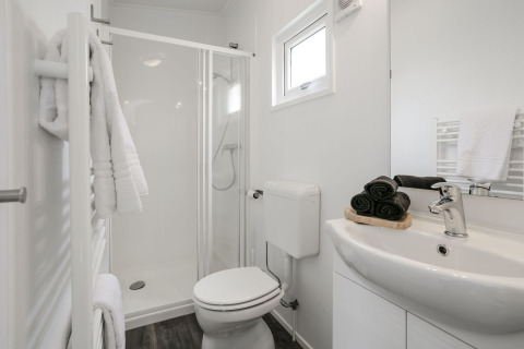 Bagno moderno con cabina doccia, accessori bianchi, asciugamani ordinati e luce naturale dalla finestra.