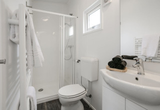 Modernes Badezimmer mit Dusche, weißer Einrichtung, Handtüchern auf dem Heizkörper und Tageslicht.