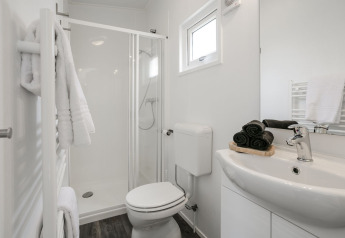 Salle de bain moderne avec douche vitrée, serviettes noires, éléments blancs et lumière naturelle.