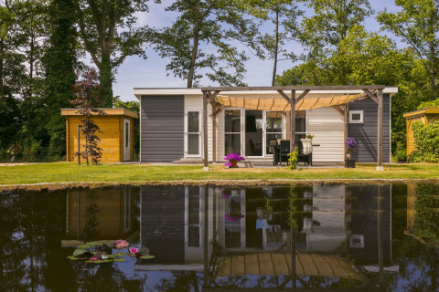 Lodge Mistique bij Holiday Park De Lochemse Berg in Nederland, met overdekt terras en vijver vooraan.