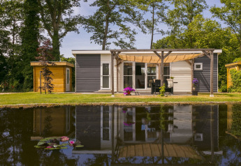 Moderne Lodge Mistique ved Holiday Park De Lochemse Berg, med overdækket terrasse og spejldam foran.