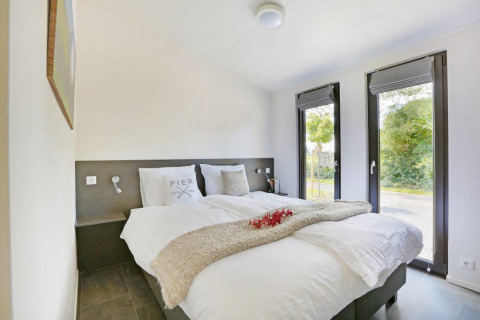 Chambre moderne avec lit double et grandes fenêtres à la Lodge Grand Modern, Holiday Park De Lochemse Berg, Pays-Bas.