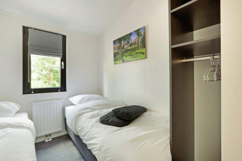 Moderne lodgeslaapkamer met twee eenpersoonsbedden, open kast en raam bij Holiday Park De Lochemse Berg, Nederland.