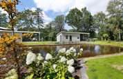 Lodge moderno con estanque, flores blancas y terraza en Holiday Park De Lochemse Berg, Países Bajos.