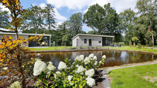 Moderne Lodge mit Teich, blühenden Pflanzen und Sitzecke im Holiday Park De Lochemse Berg, Niederlande.