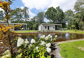 Moderne Lodge mit Teich, blühenden Pflanzen und Sitzecke im Holiday Park De Lochemse Berg, Niederlande.