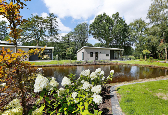 Moderne lodge met vijver, witte bloemen en terras in Holiday Park De Lochemse Berg, Nederland.