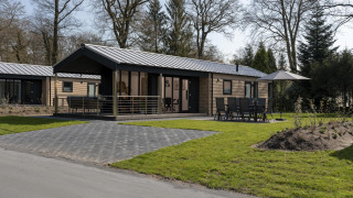 Lodge moderne au Holiday Park De Lochemse Berg aux Pays-Bas, avec terrasse, chaises et jardin vert.