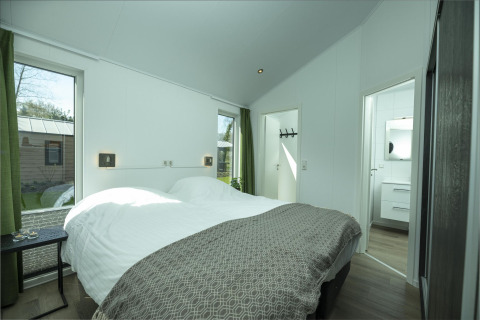 Dormitorio luminoso con cama doble, grandes ventanas y cortinas verdes en Terrace Lodge, Holiday Park De Lochemse Berg.