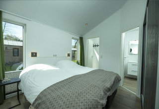 Chambre lumineuse avec lit double, grandes fenêtres et rideaux verts au Terrace Lodge, Holiday Park De Lochemse Berg.