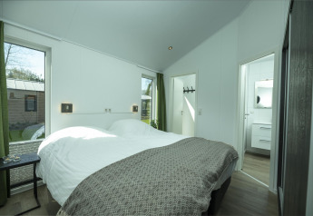 Chambre lumineuse avec lit double, grandes fenêtres et rideaux verts au Terrace Lodge, Holiday Park De Lochemse Berg.