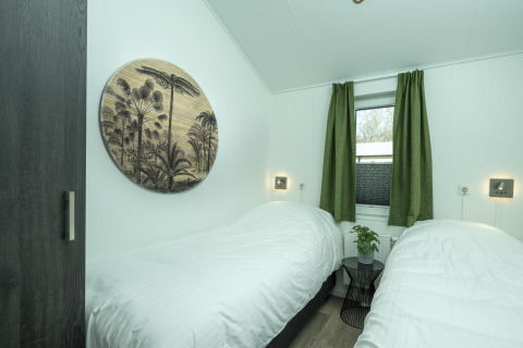 Schlafzimmer in der Terrace Lodge im Holiday Park De Lochemse Berg mit zwei Betten, grünen Vorhängen und Wandkunst.