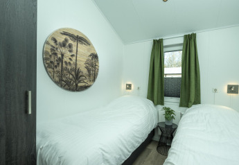 Slaapkamer in Terrace Lodge bij Holiday Park De Lochemse Berg met twee bedden, groene gordijnen en muurdecoratie.