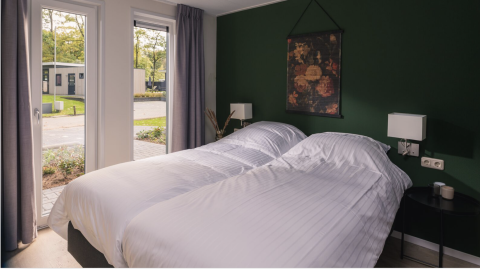 Dormitorio moderno con dos camas, ropa de cama blanca y ventanales en Kubus Lodge, Holiday Park De Lochemse Berg, Países Bajos.