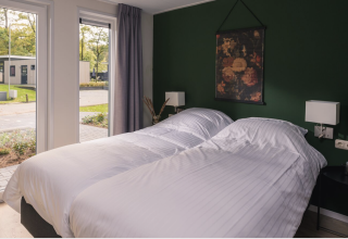 Dormitorio moderno con dos camas, ropa de cama blanca y ventanales en Kubus Lodge, Holiday Park De Lochemse Berg, Países Bajos.