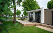Moderna cabaña llamada Villa Maritiem con terraza de madera, bicicletas y sillas de jardín entre árboles verdes.