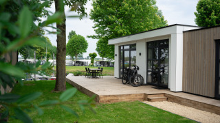 Moderne lodge genaamd Villa Maritiem met houten terras, fietsen en tuinmeubilair, omringd door bomen.