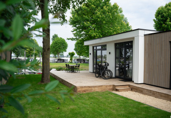 Moderna cabaña llamada Villa Maritiem con terraza de madera, bicicletas y sillas de jardín entre árboles verdes.