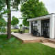 Moderna cabaña llamada Villa Maritiem con terraza de madera, bicicletas y sillas de jardín entre árboles verdes.