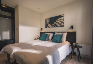 Habitación moderna en Villa Maritiem con cama doble, cojines azules y cuadro de barcos en la pared.