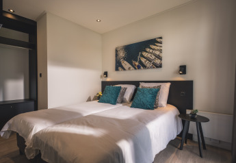 Habitación moderna en Villa Maritiem con cama doble, cojines azules y cuadro de barcos en la pared.