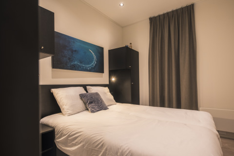Moderne soveværelse på Villa Maritiem lodge med dobbelt seng, hvide lagner, sort indretning og maritimt kunstværk.