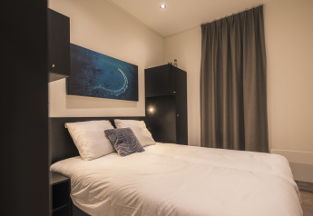 Moderne slaapkamer bij Villa Maritiem lodge met tweepersoonsbed, witte lakens, donker meubilair en zee-kunstwerk.