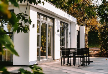Moderne lodge ved MarinaPark Bad Nederrijn i Holland, omgivet af grønne træer og terrasse med havemøbler.