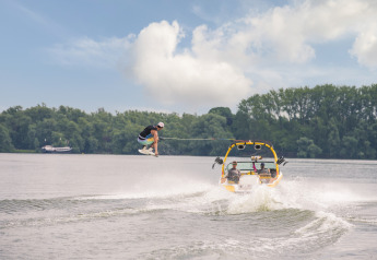 Wakeboard en el lago frente a Villa Maritiem Lodge, con vegetación de fondo y barco remolcando al deportista.