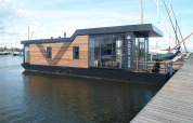 Moderne husbåd ved kajen på Waterlodge 4, Zuiderzee, Holland, med træpaneler og store vinduer.