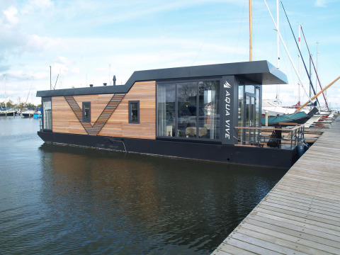 Moderne woonboot aangemeerd aan de steiger van Waterlodge 4 te Zuiderzee, Nederland, met houten gevel.