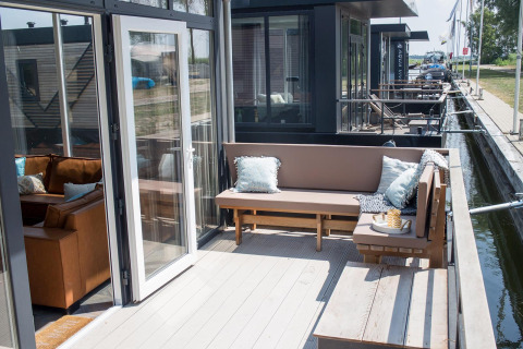Terrasse mit Sitzbank und Kissen auf Waterlodge 4 am Zuiderzee in den Niederlanden, Blick auf Kanal.